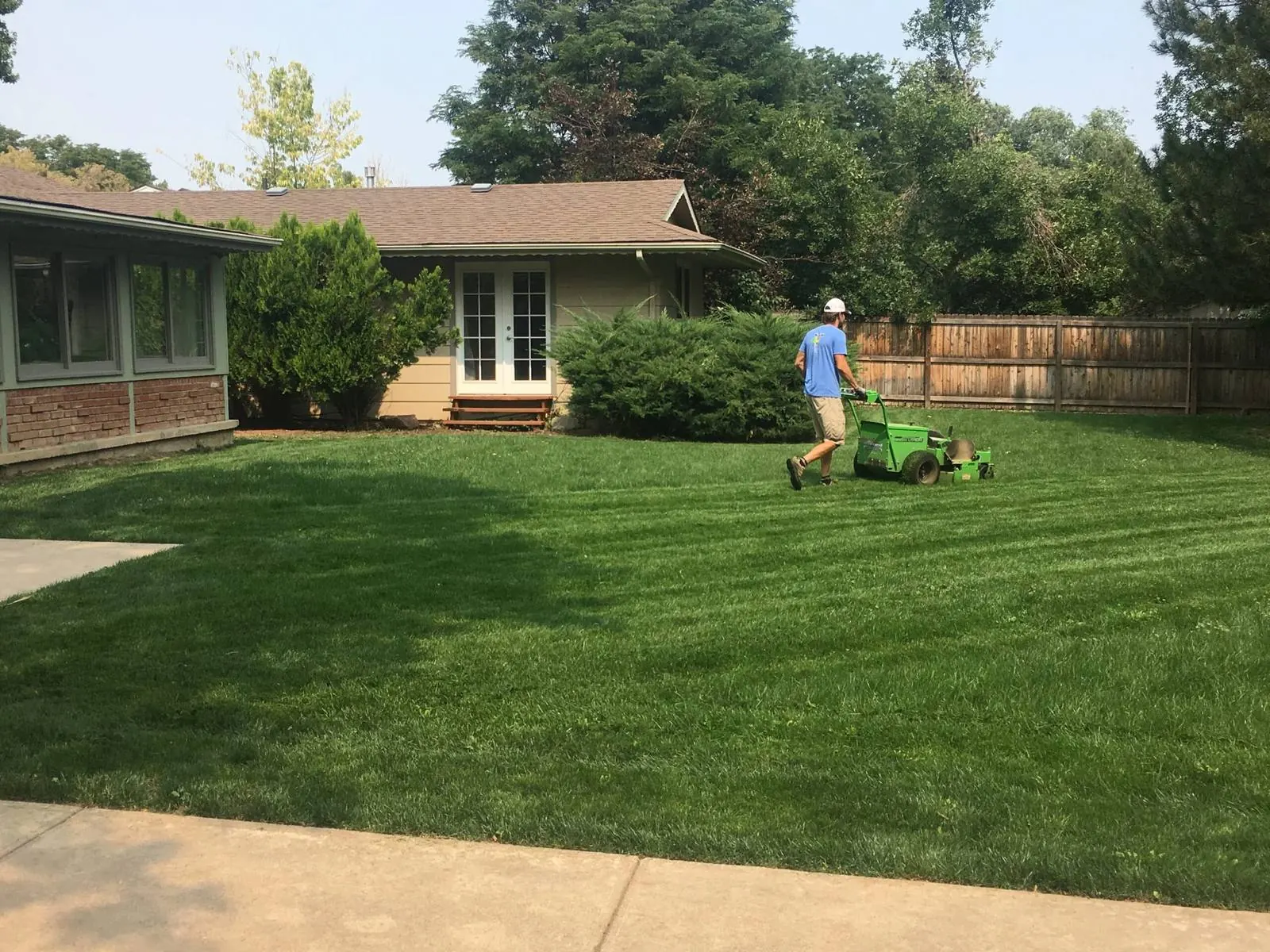 Lawn care worker mowing a large green residential backyard